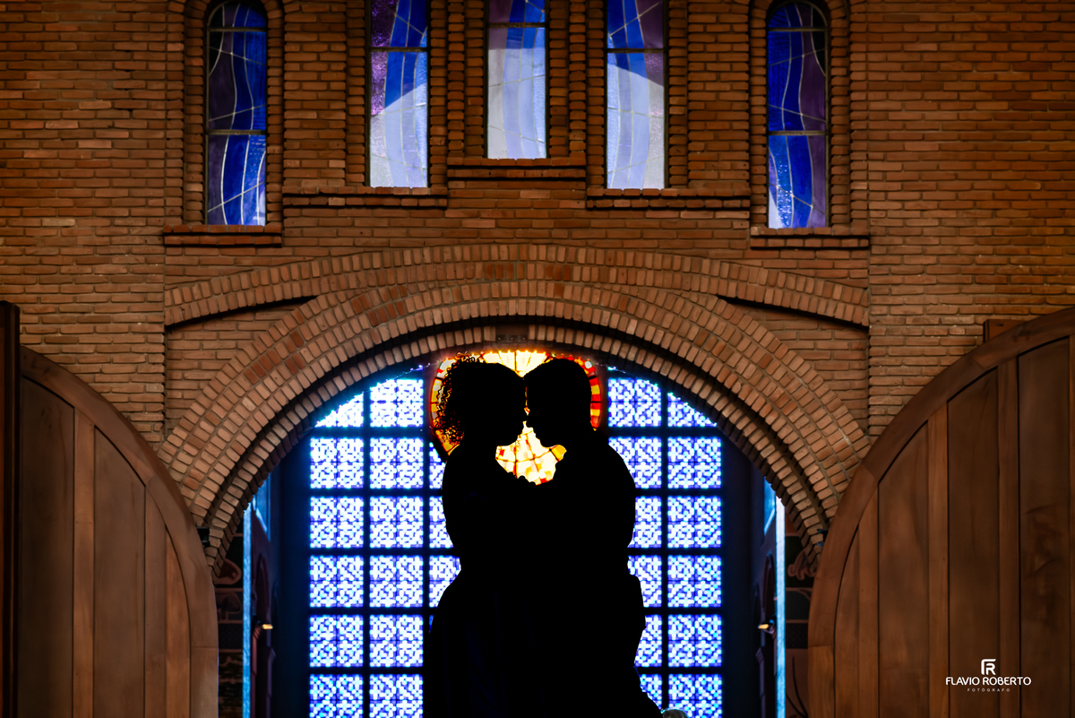 Silhueta de casal em ensaio pré wedding no Santuário Nacional de Aparecida com vitral iluminado ao fundo