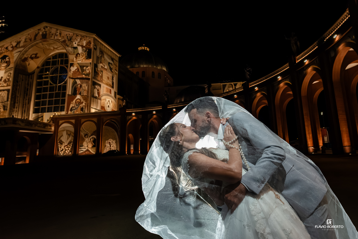 Beijo dos noivos sob o véu durante ensaio noturno no Santuário Nacional de Aparecida