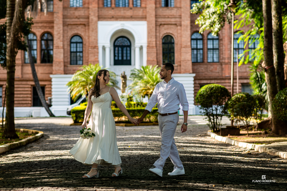 Casal caminhando em frente à fachada principal da Pousada Bom Jesus em Aparecida durante ensaio pré wedding
