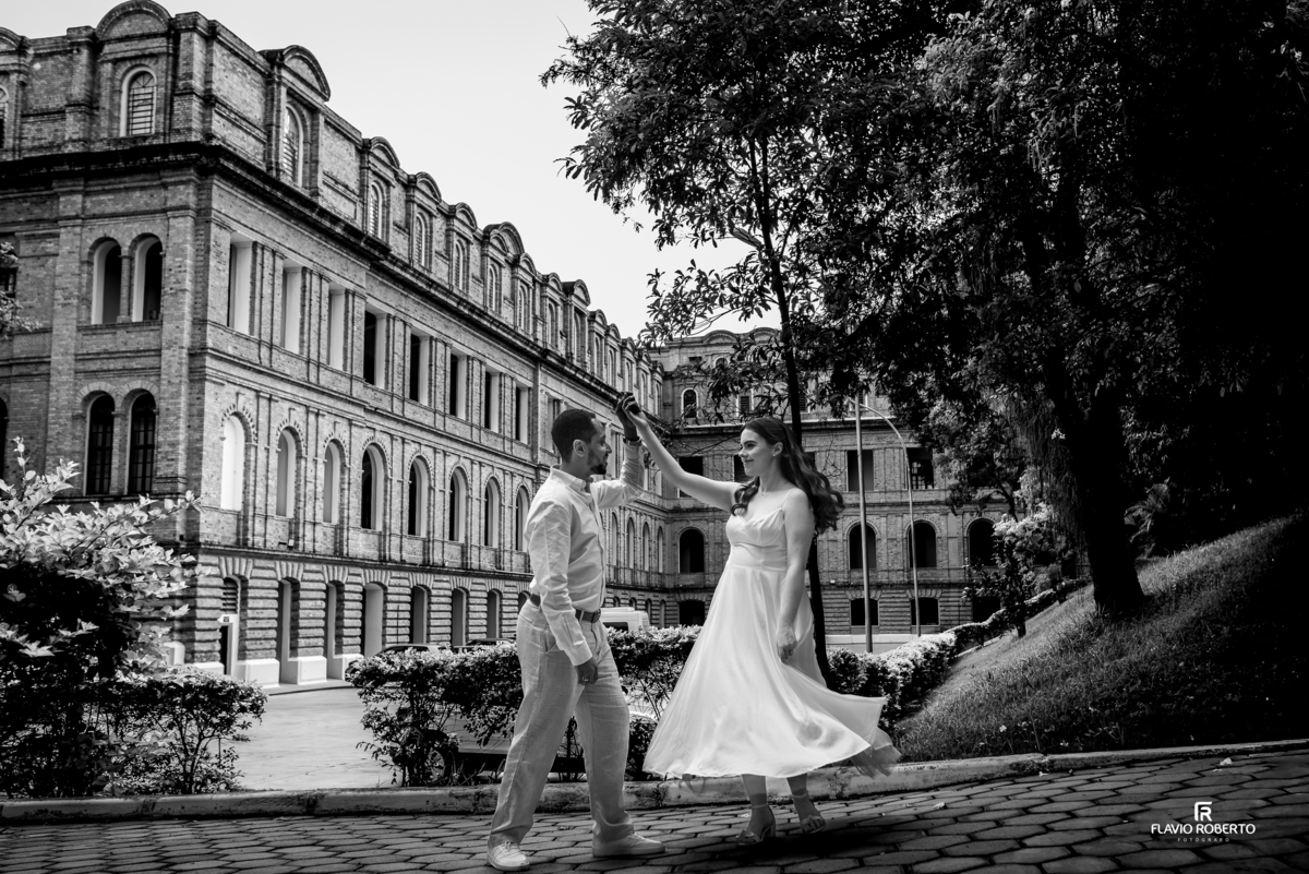 Foto em preto e branco do casal em movimento com arquitetura histórica da Pousada Bom Jesus em Aparecida ao fundo