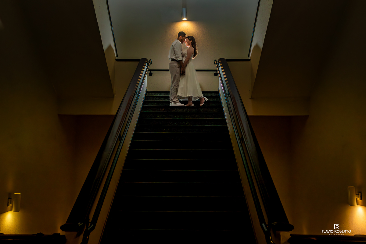 Casal em pé na escada com iluminação dramática no Seminário Bom Jesus em Aparecida