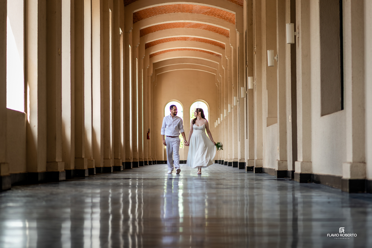 Casal caminhando de mãos dadas em corredor histórico do Seminário Bom Jesus em Aparecida durante ensaio pré wedding