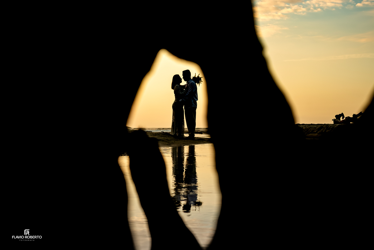 Casal fotografado entre troncos na praia de Ubatumirim