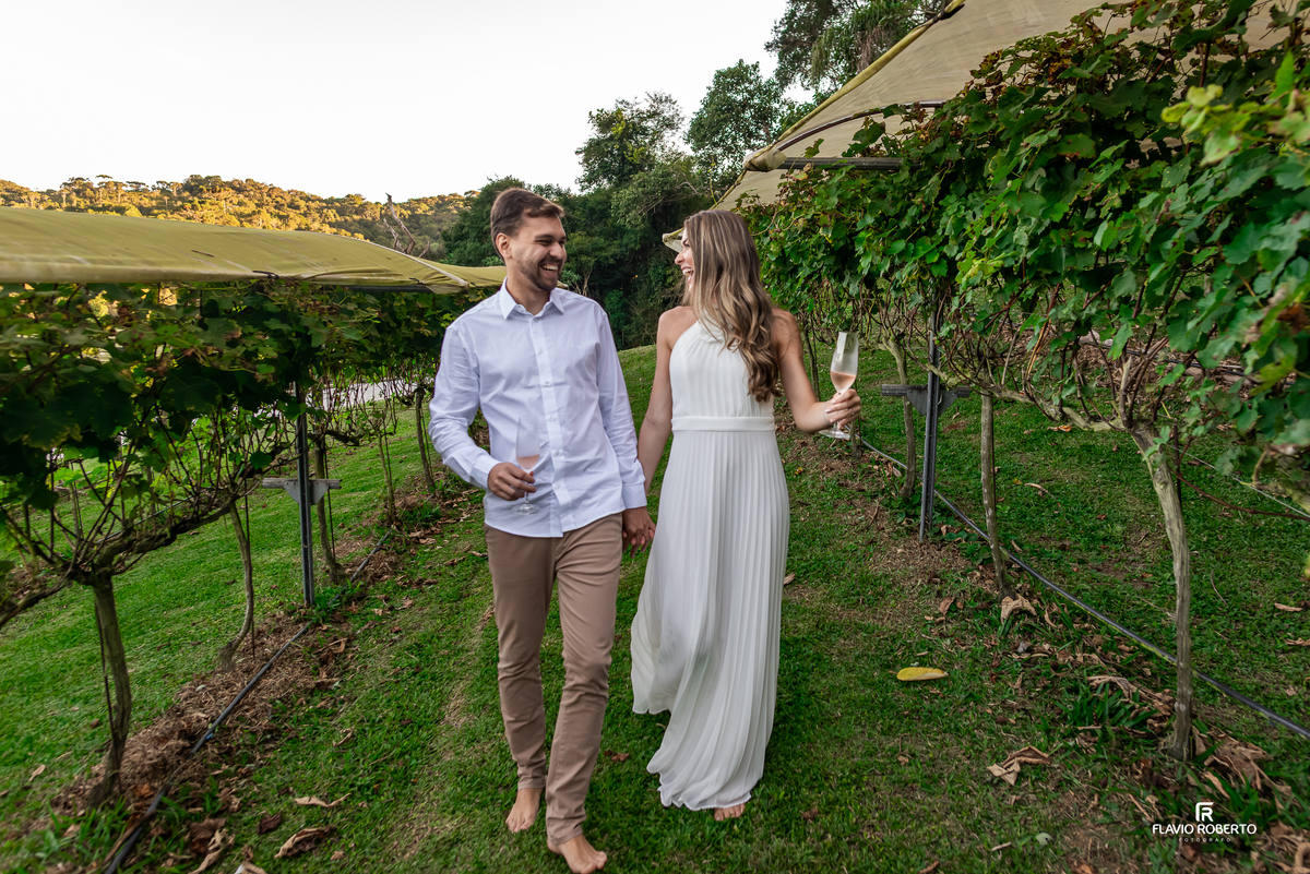 Casal caminhando entre os vinhedos com taças de vinho durante pré wedding na Vinícola Essenza.