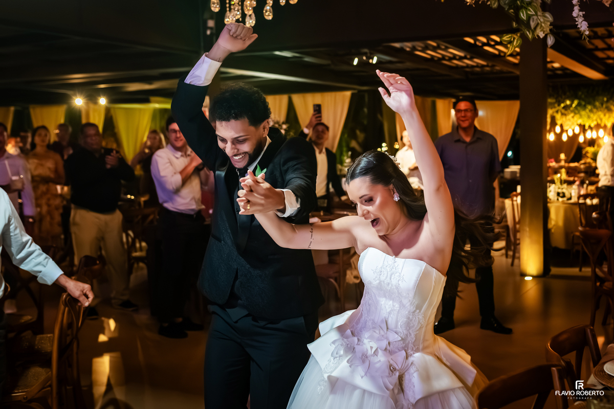 Noivos comemorando e dançando com muita alegria durante a festa de casamento no Sítio Tangaroa em Taubaté, cercados por familiares e amigos.