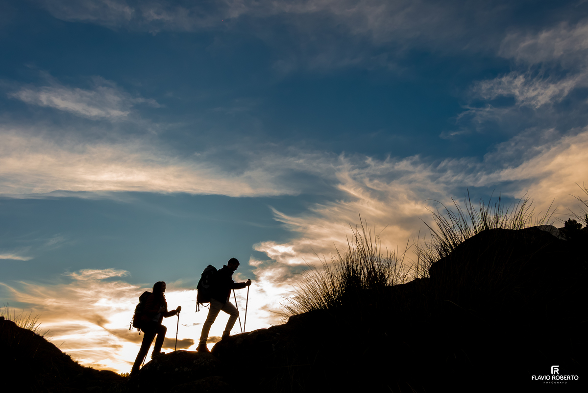 Silhueta de casal caminhando por trilha ao pôr do sol no Pico das Agulhas Negras.