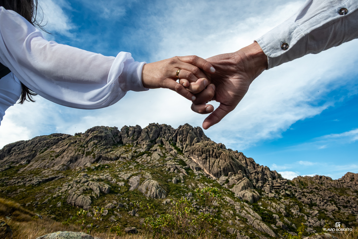 Mãos entrelaçadas do casal com o Pico das Agulhas Negras ao fundo.