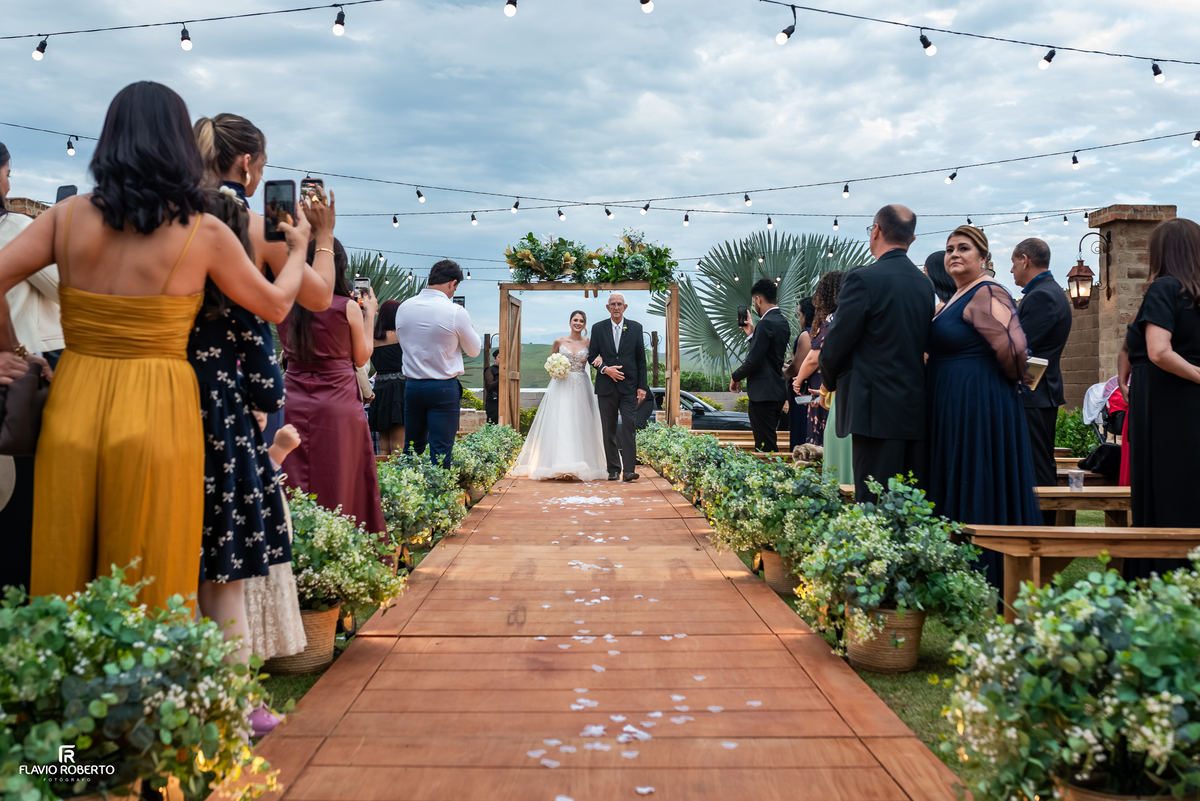 Entrada da noiva Júlia acompanhada do pai durante a cerimônia de casamento no Espaço Aloha em Cruzeiro/SP.