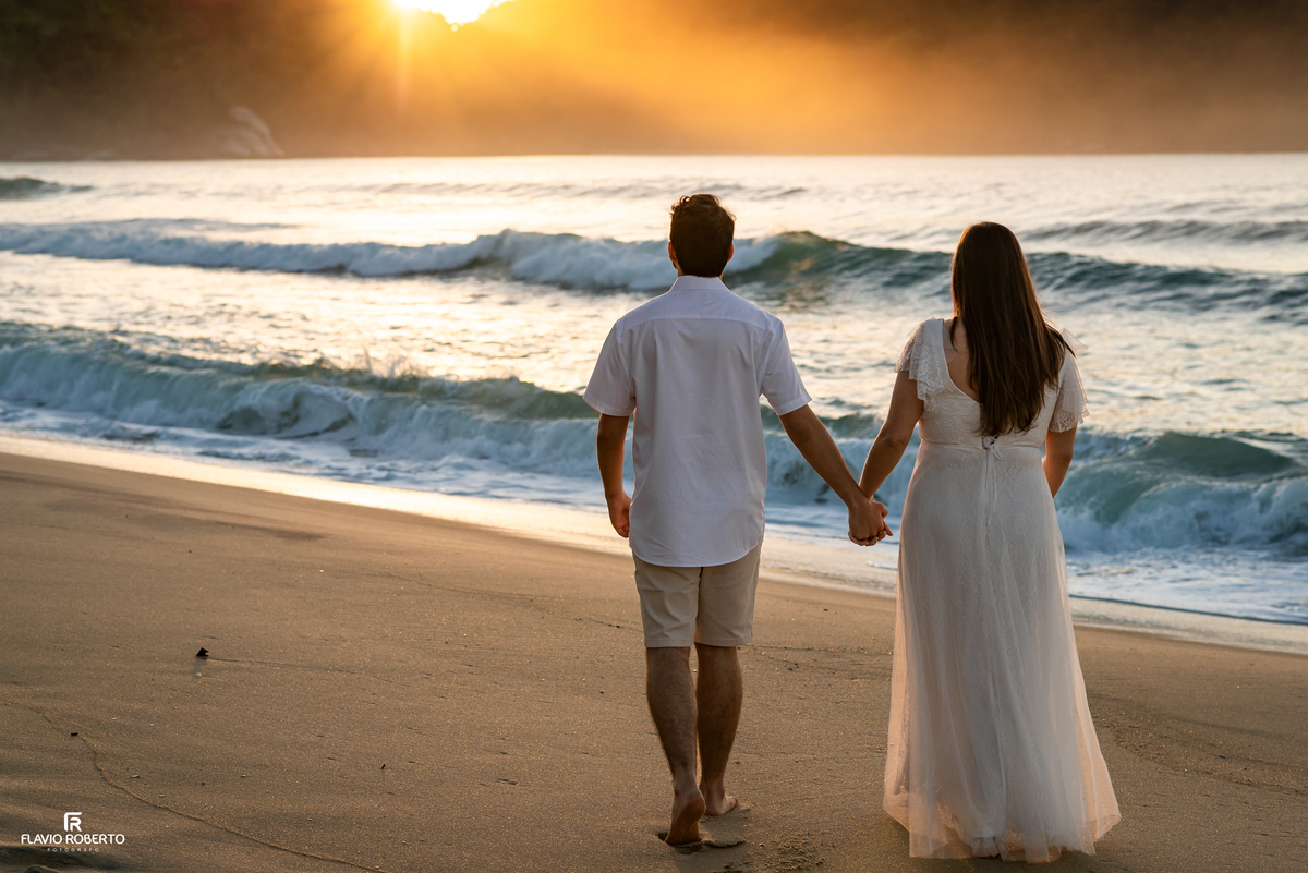 Casal caminhando de mãos dadas pela praia durante o nascer do sol em Ubatuba.