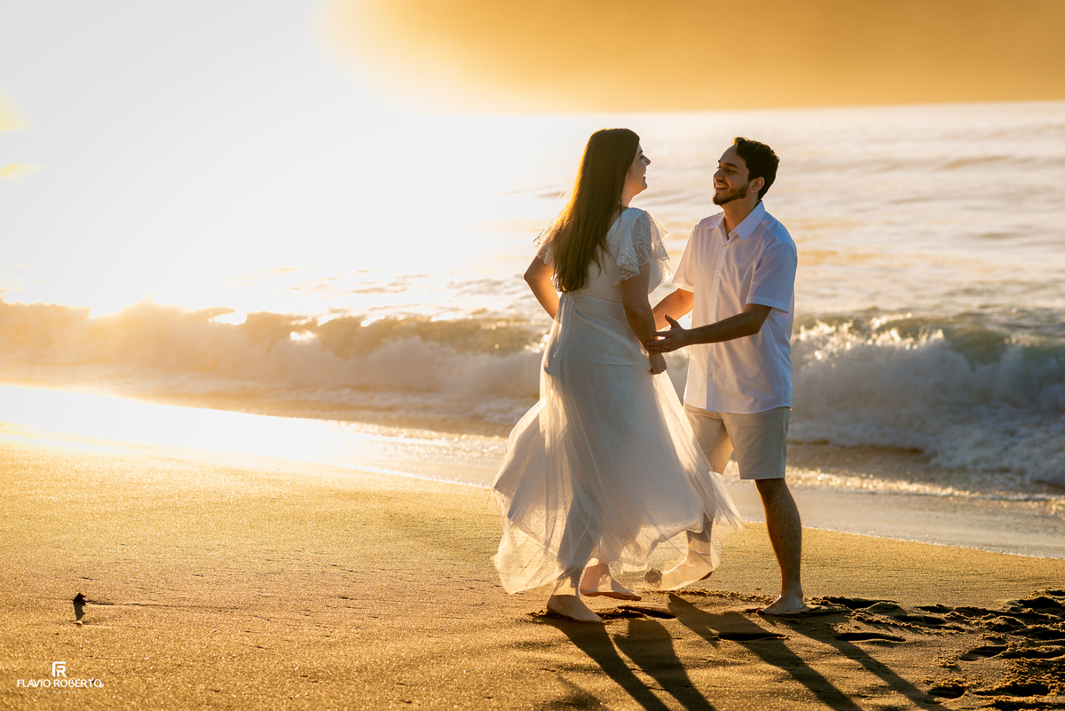 Casal sorrindo enquanto brinca na areia durante ensaio ao amanhecer.