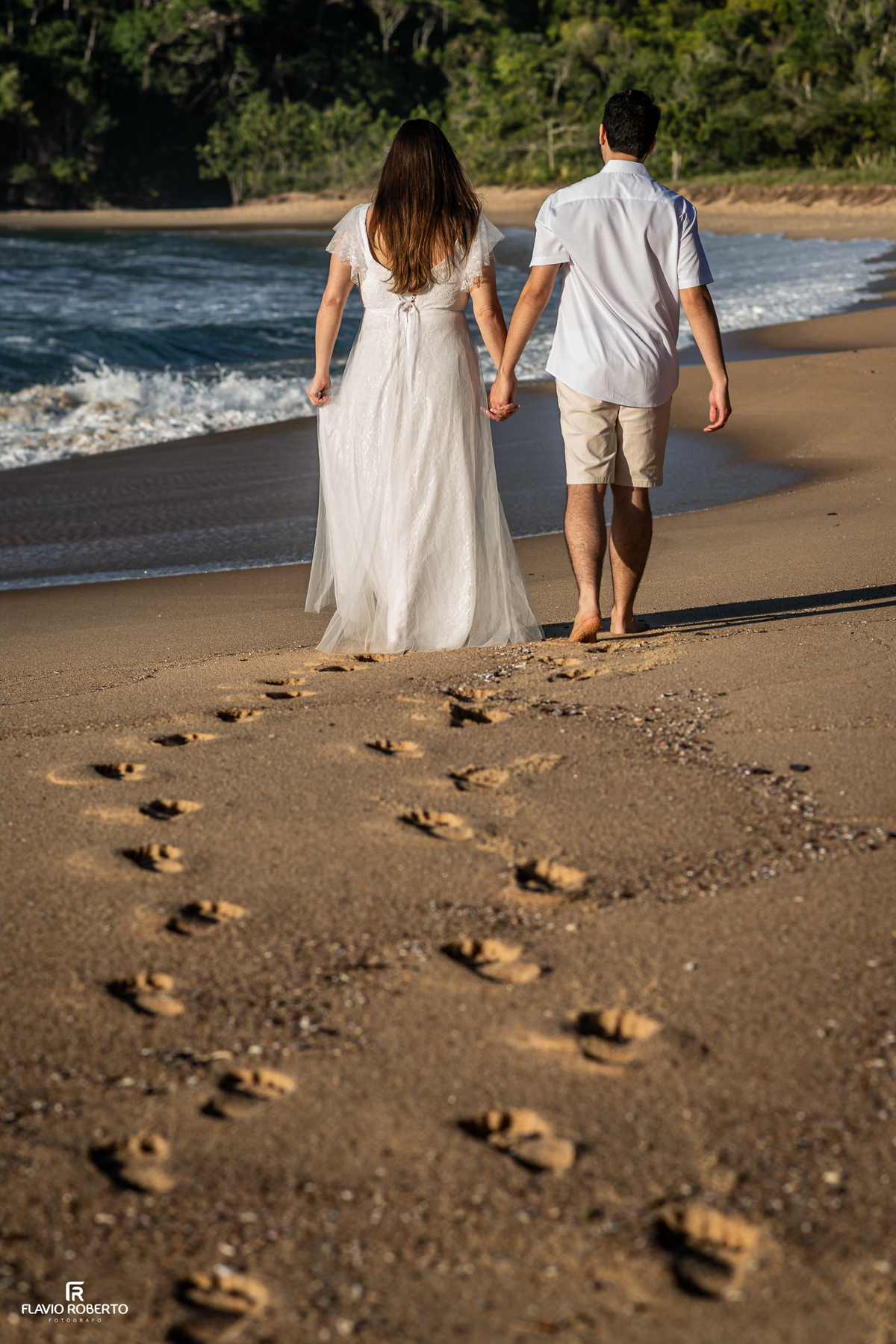 Casal caminhando de mãos dadas pela areia durante ensaio pré wedding na Praia Vermelha do Norte, em Ubatuba.