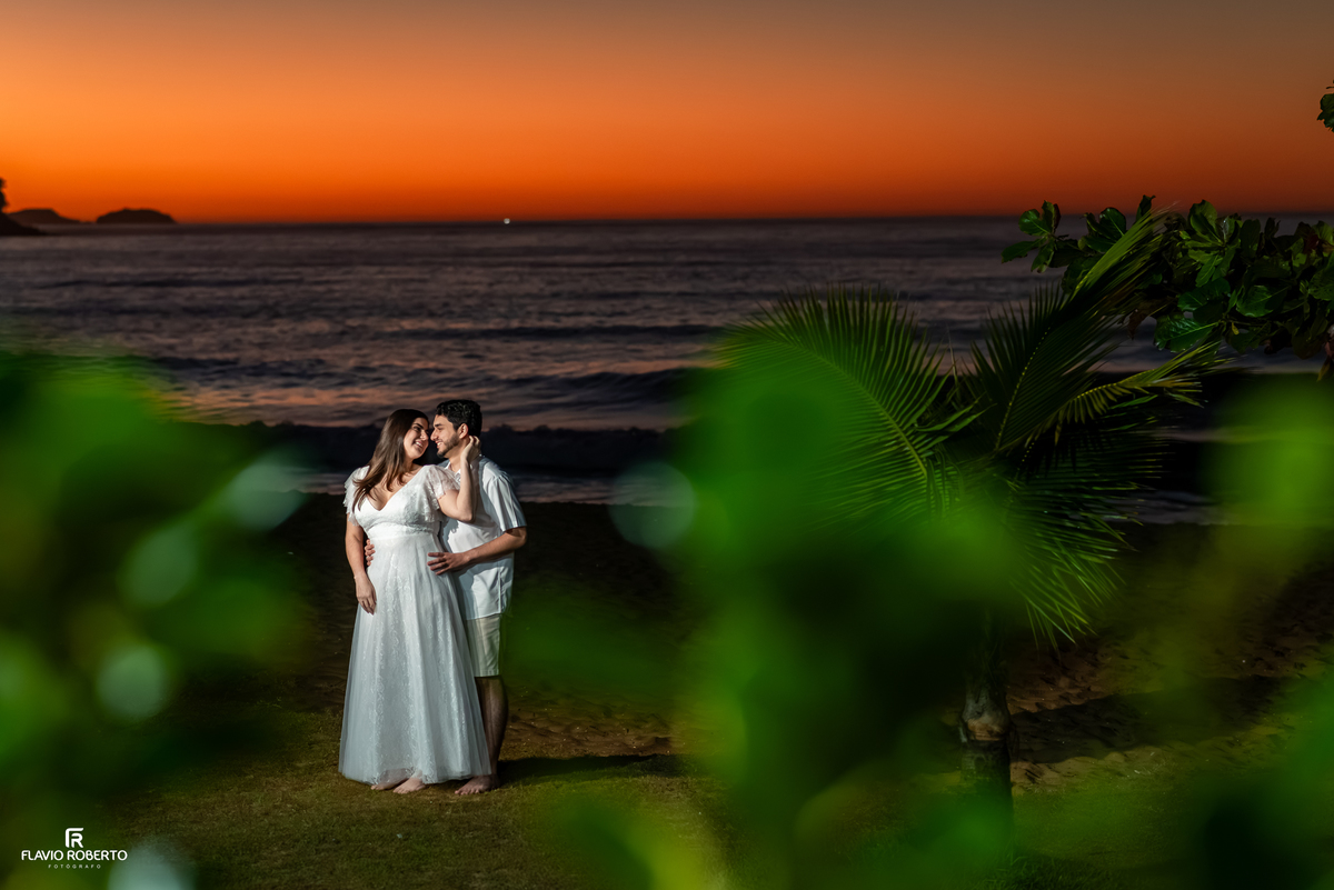 Casal fotografado entre a vegetação com o céu alaranjado antes do nascer do sol na Praia Vermelha do Norte, em Ubatuba.