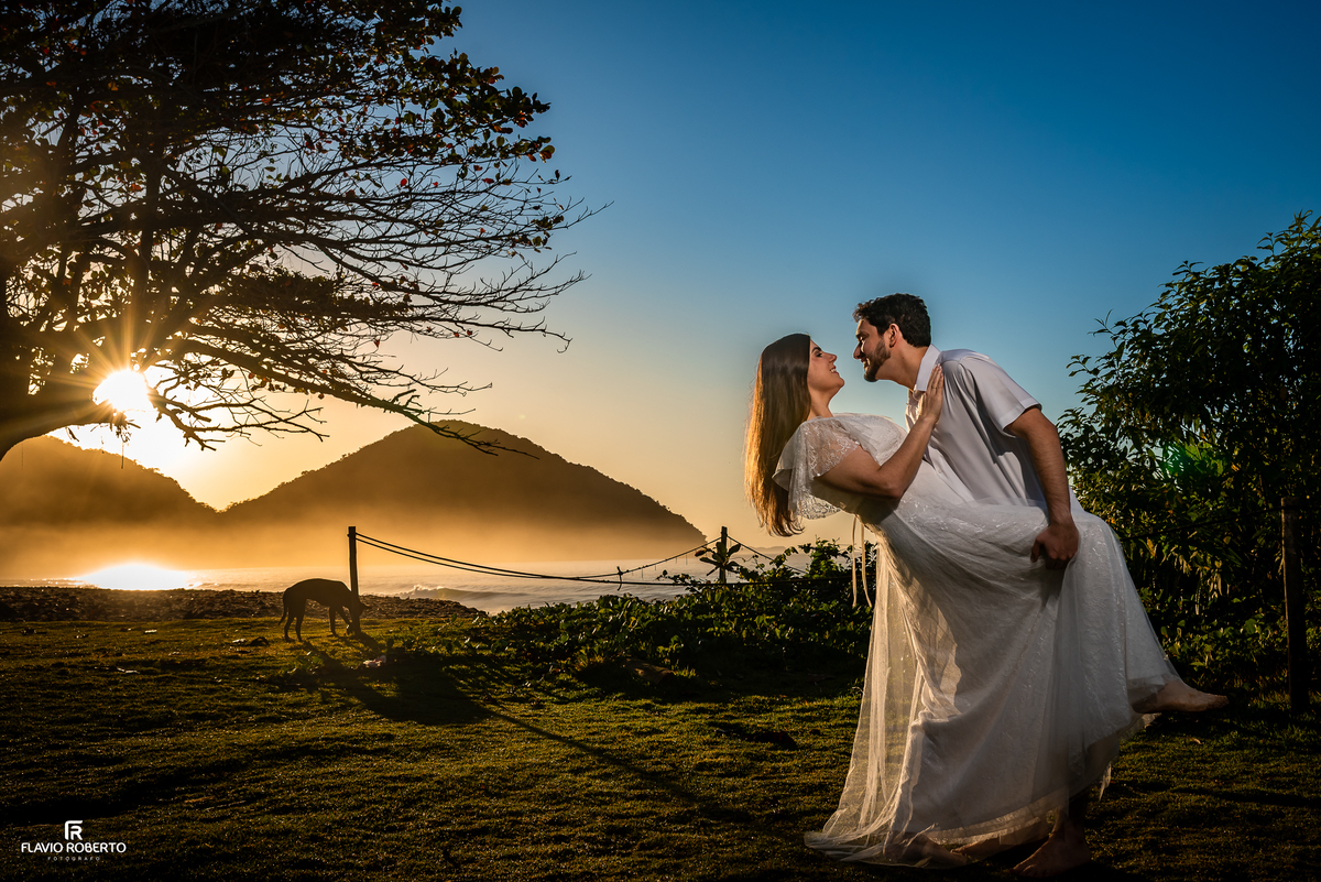 Noivo segura a noiva durante ensaio pré wedding ao pôr do sol na Praia Vermelha do Norte, em Ubatuba.