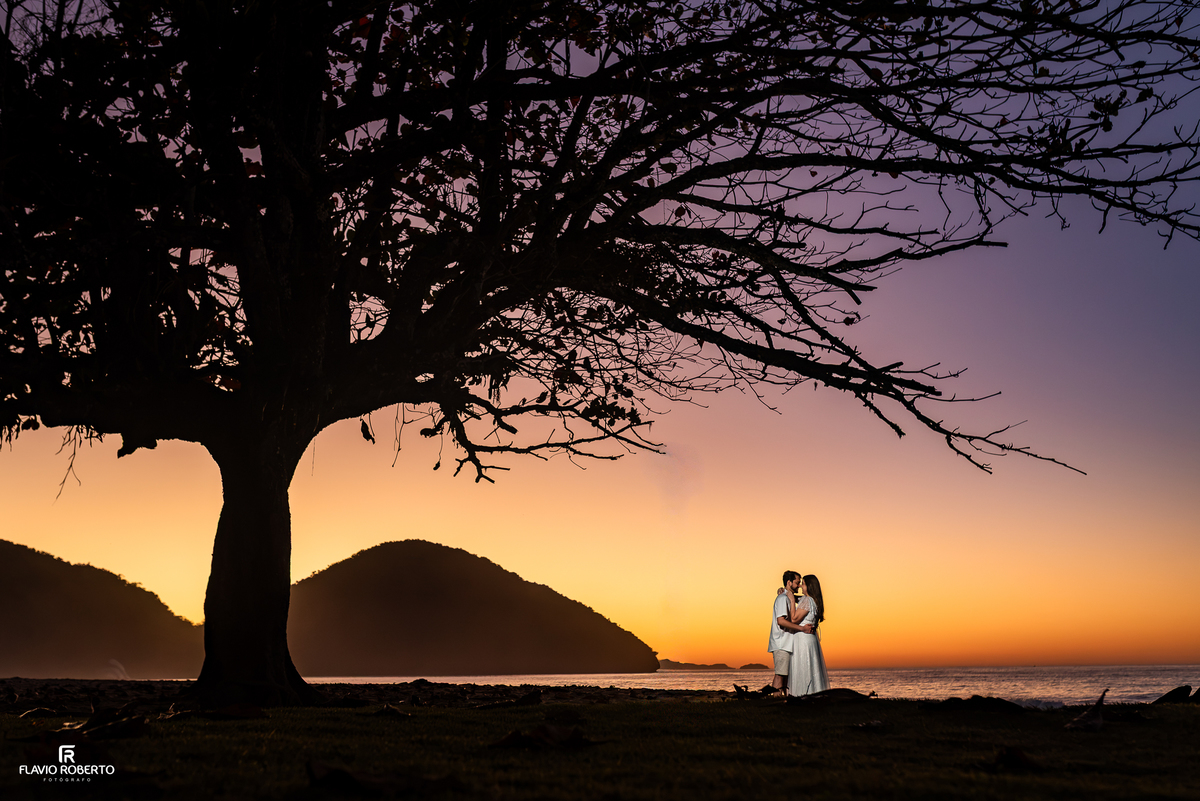 Natália e Kauan em ensaio romântico sob uma árvore na Praia Vermelha do Norte ao amanhecer.