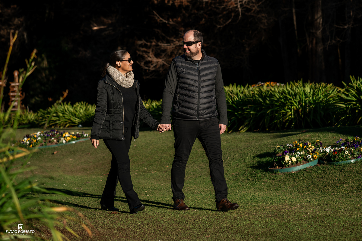Casal caminhando pelos jardins do Horto Florestal de Campos do Jordão durante ensaio fotográfico.