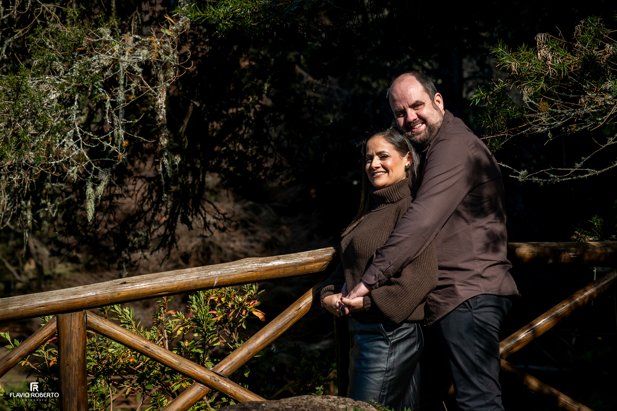 Marcilene e Paulo abraçados sobre uma ponte de madeira durante ensaio fotográfico no Horto Florestal de Campos do Jordão.