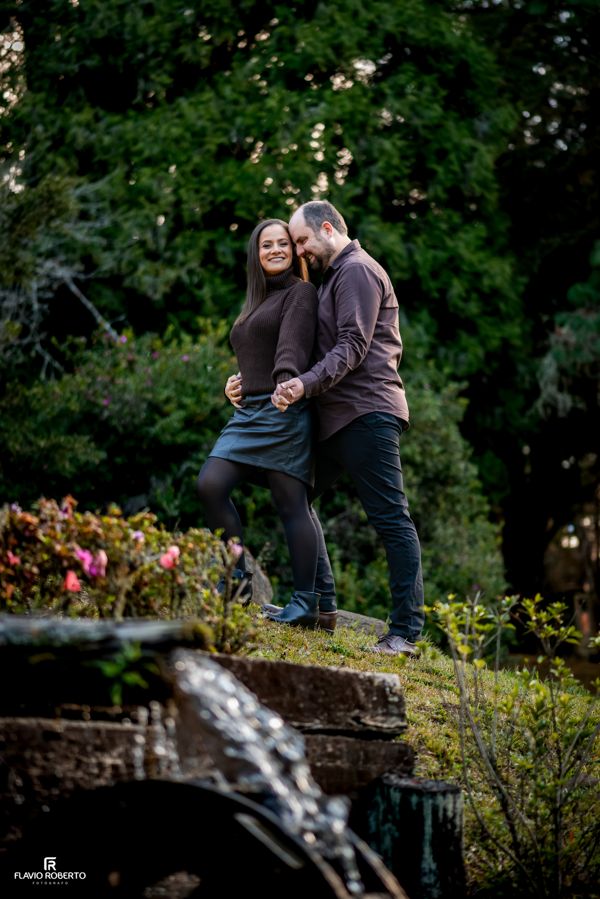 Fotografia ampla do casal junto à roda d'água no Parque Estadual de Campos do Jordão.
