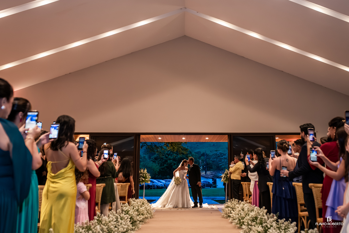 Pai beija a filha na entrada da cerimônia de casamento no Recanto do Bosque, em Guaratinguetá, com convidados ao redor.