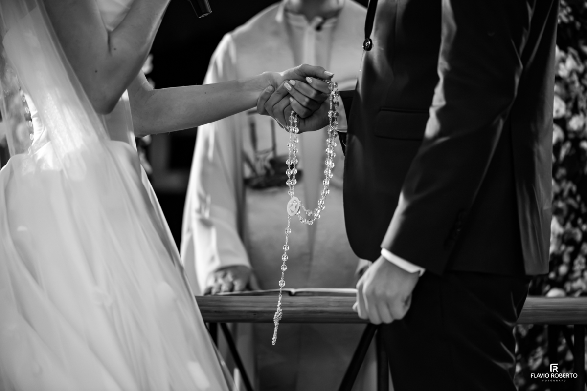 Noivos de mãos dadas segurando um terço durante cerimônia católica de casamento em Guaratinguetá.