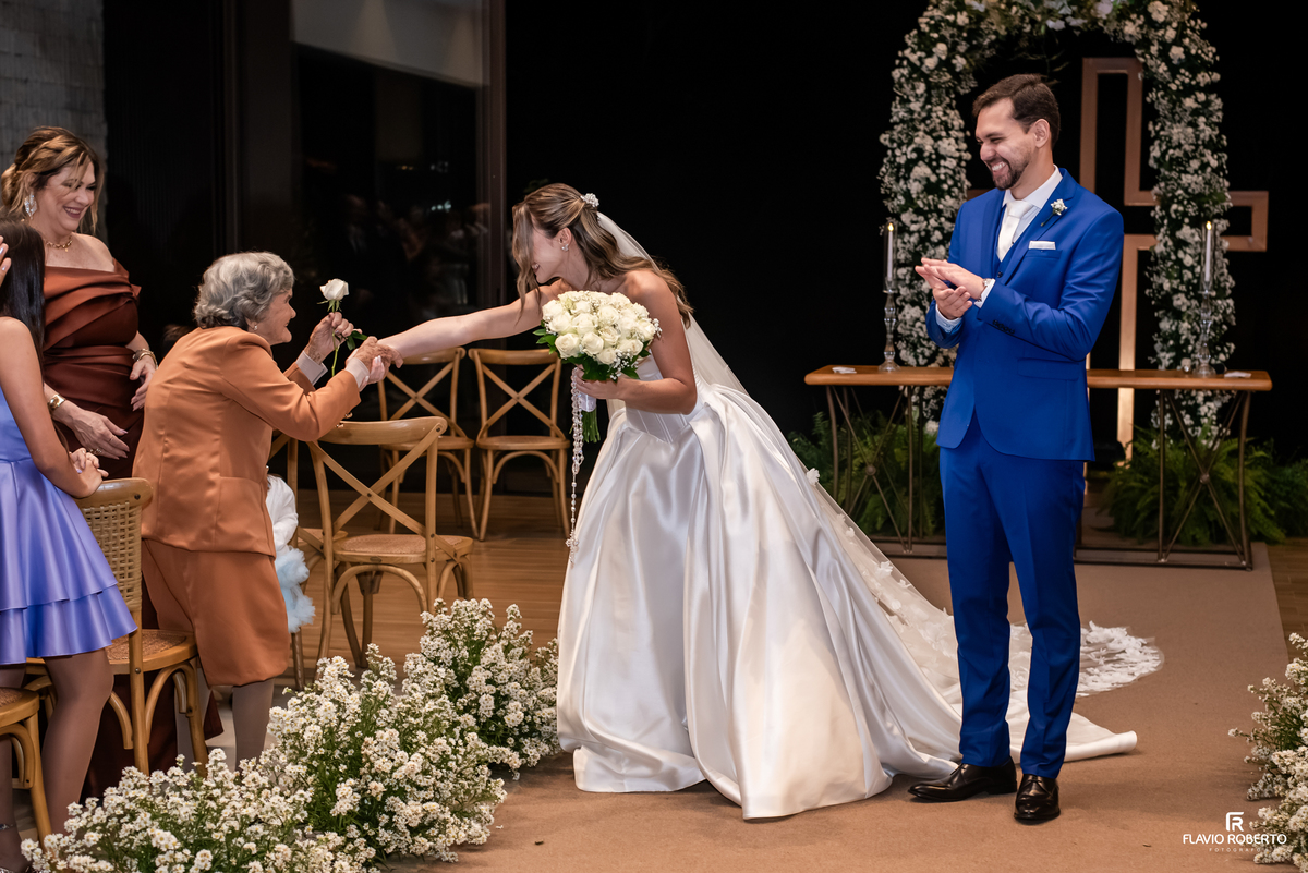 Noiva recebe uma rosa de senhora idosa enquanto o noivo aplaude durante casamento no Recanto do Bosque.