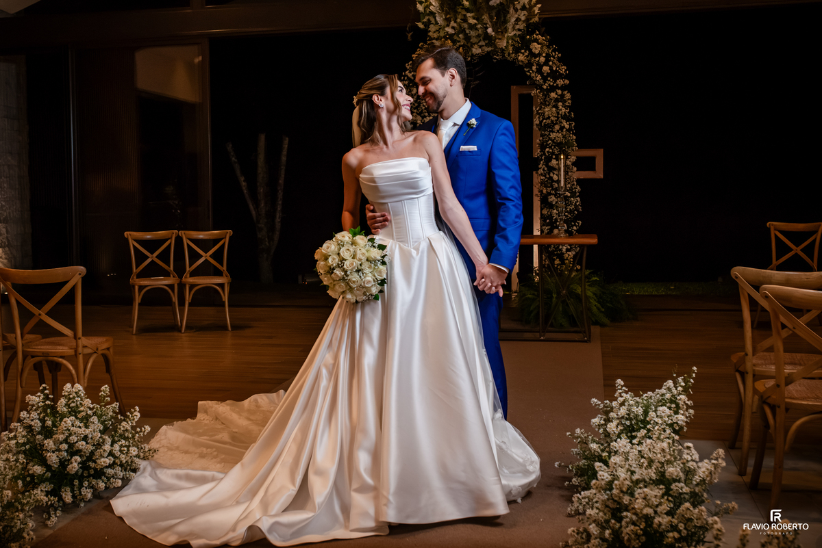 Noivos de mãos dadas e sorrindo em retrato após casamento no Recanto do Bosque, em Guaratinguetá.