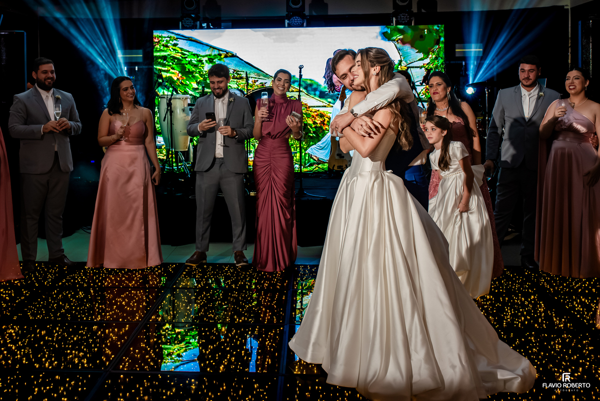 Noivo abraça e beija a noiva na pista de dança durante recepção de casamento no Recanto do Bosque.