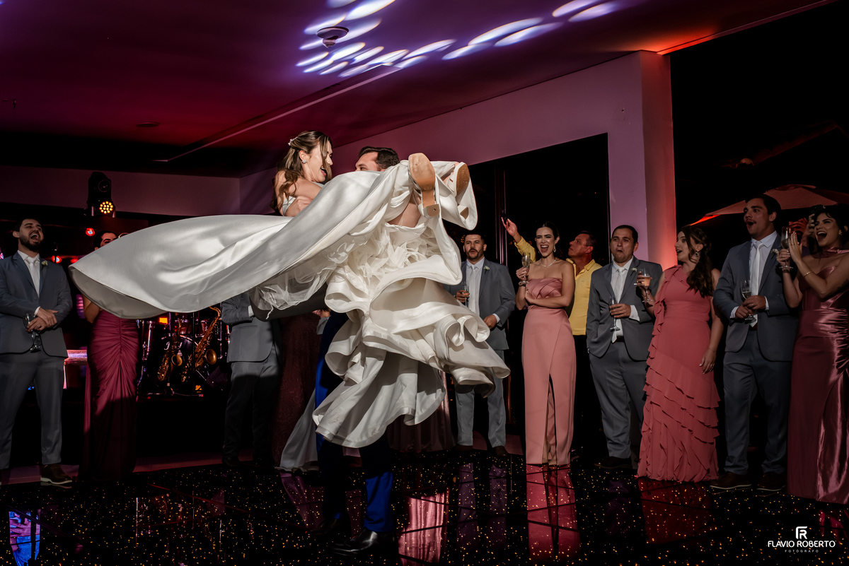 Noivo beija a noiva durante dança animada diante dos convidados na festa de casamento no Recanto do Bosque.