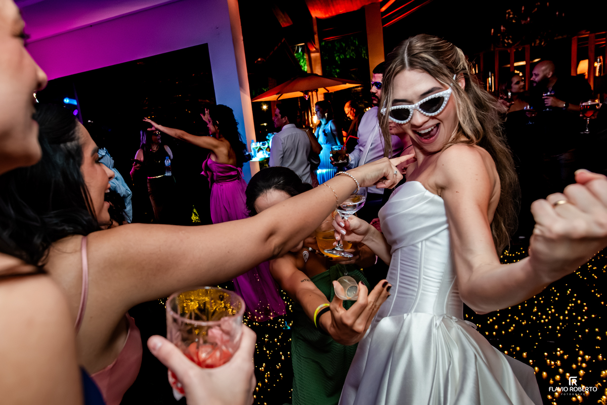 Noiva de óculos divertidos dançando com convidadas durante festa de casamento no Recanto do Bosque