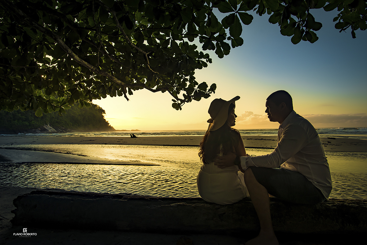 namorados sentados em baixo de uma árvore vendo o sol nascer na praia, durante Ensaio Pre Wedding em Ubatuba