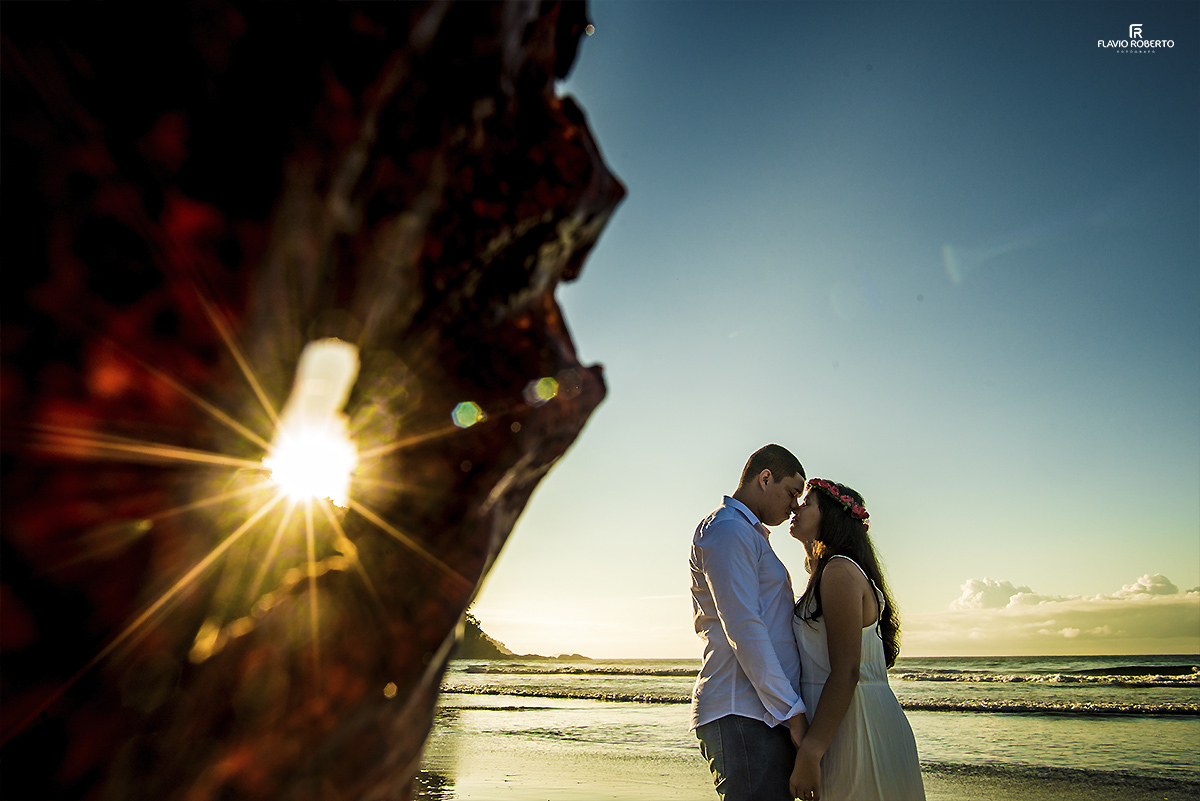 casal se beijando na praia com o sol refletindo no buraco de uma folha de árvore
