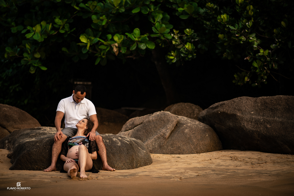 Casal de gestante conversando na praia, sentados numa pedra