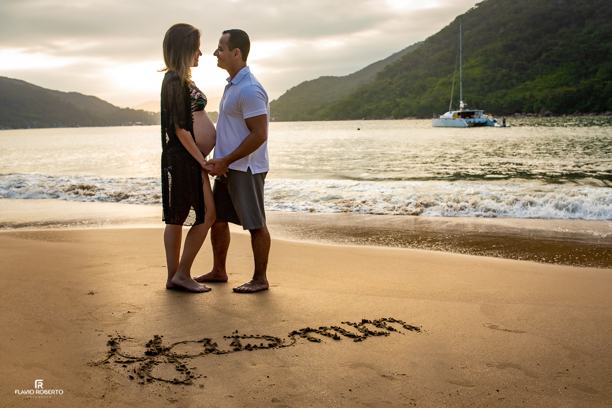 Casal abraçado na praia com o nome da filha escrito na areia da Praia Santa Rita em Ubatuba(SP)