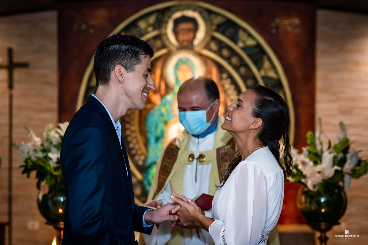 noiva sorrindo colocando a aliança no dedo do Noivo