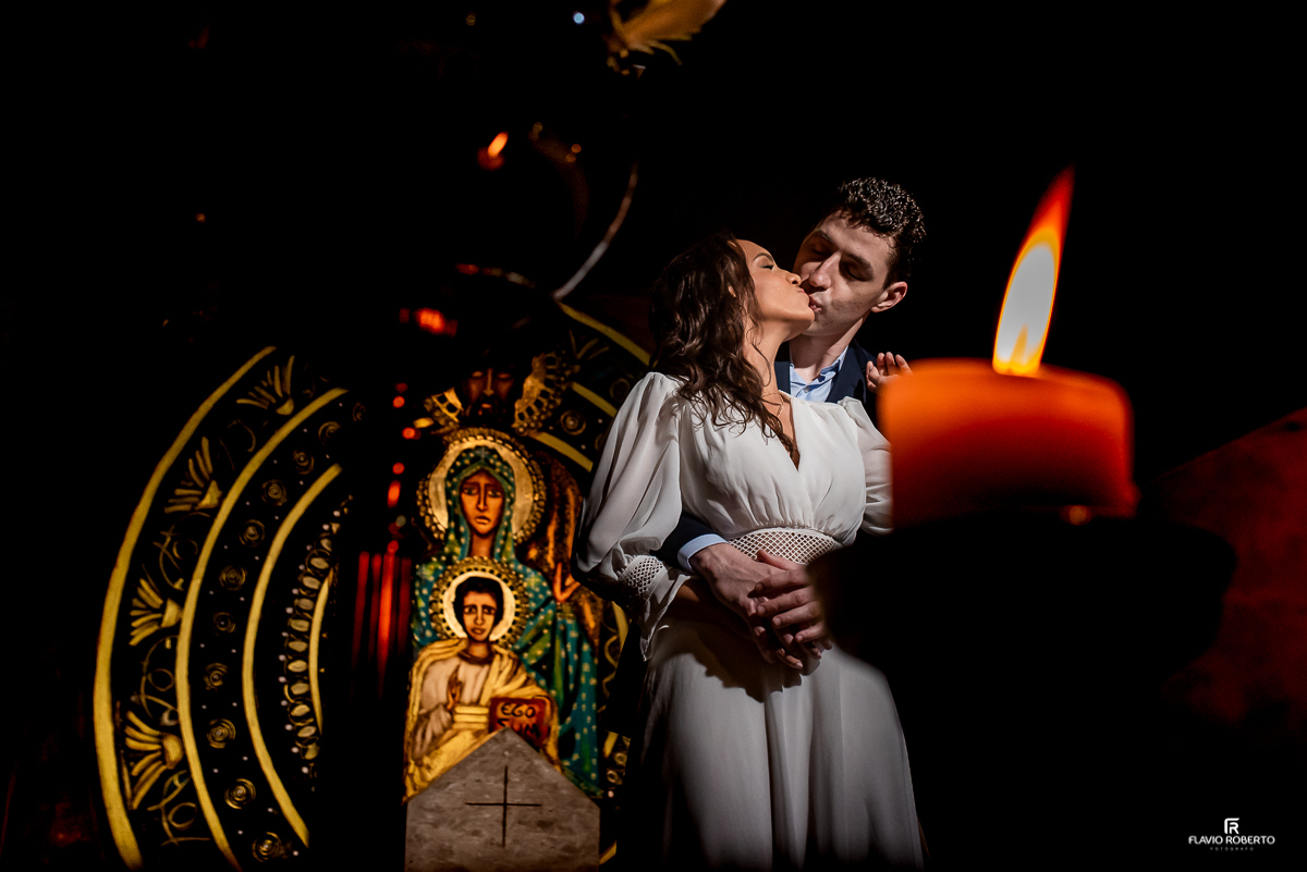 noivos se beijando próximo de uma vela, na frente do ícone da Sagrada Família na Paróquia Sao Luiz Gonzaga em SP