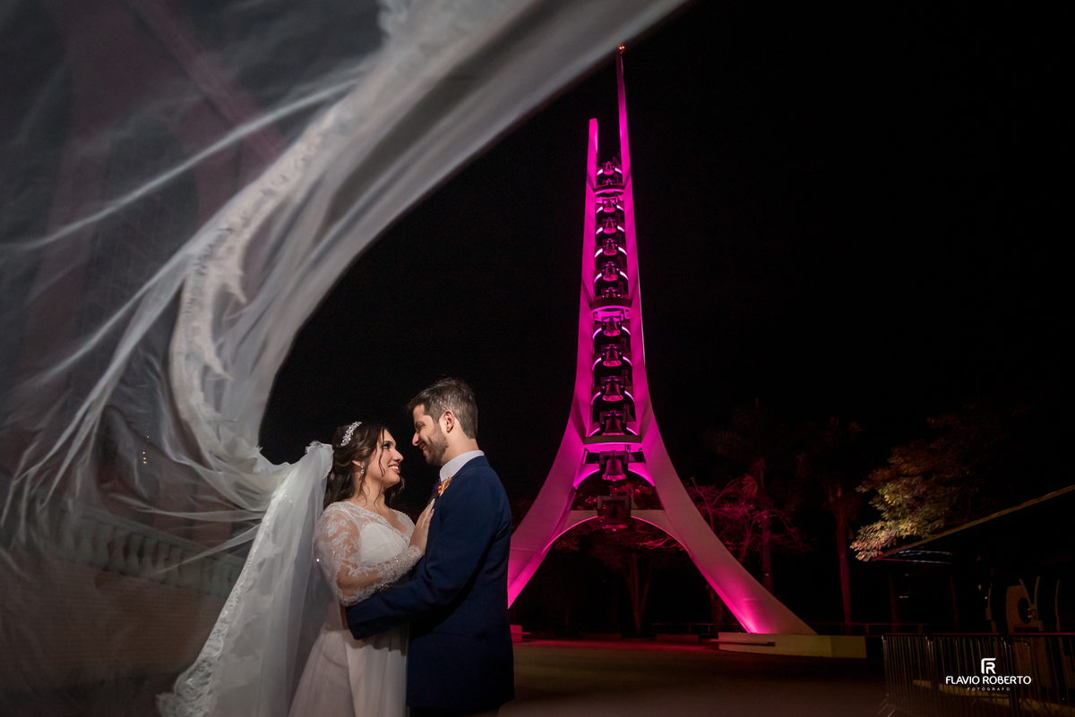 Casal de noivos em ensaio noturno romântico em Aparecida do Norte com véu em movimento e Campanário do Santuário iluminada