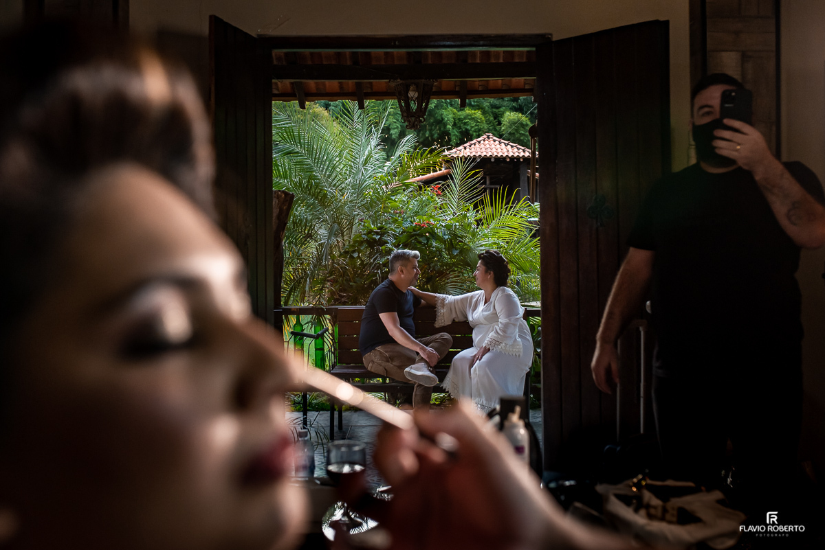 Noiva maquiando enquanto seus pais conversam.