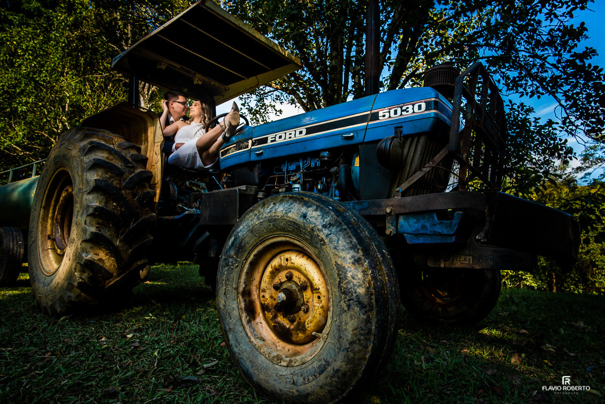 Casal sentado em um trator dando risada durante Ensaio Pre Wedding no Recanto do Bosque em Guaratinguetá.