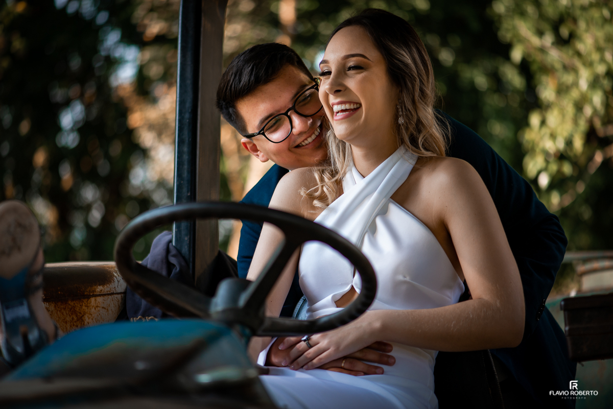 Casal sentado em um trator dando risada durante Ensaio Pre Wedding no Recanto do Bosque em Guaratinguetá.