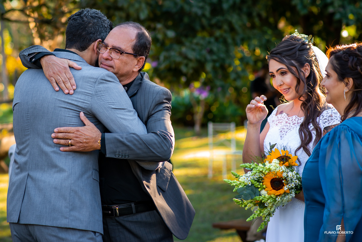 Pai da noiva abraçando seu genro sob os olhares de sua esposa e sua filha
em Casamento realizado no Sítio dos Ipês em Taubaté