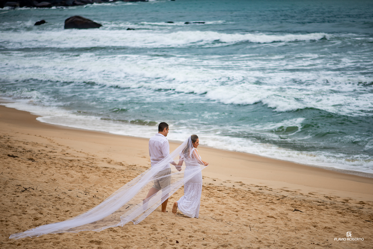 Noiva caminhando com seu noivo pela praia vermelha em Ubatuba, com seu véu voando durante ensaio pre wedding em ubatuba