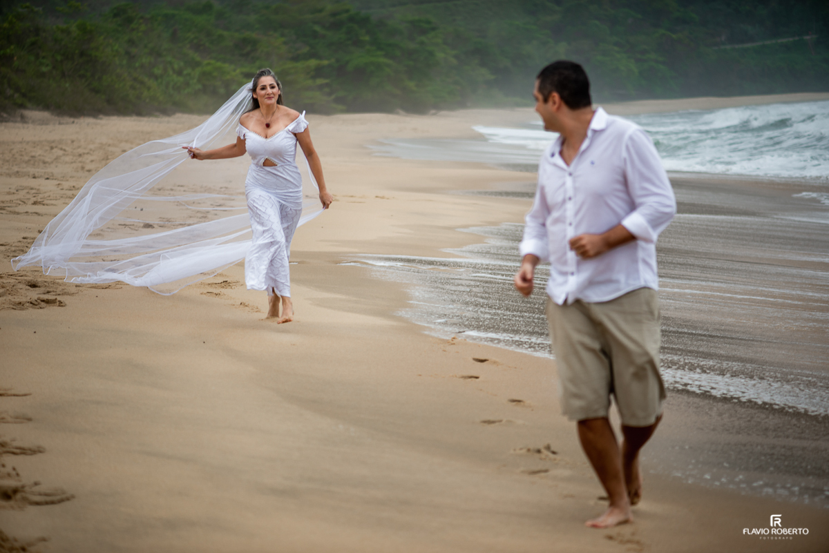 Noiva correndo atrás do seu noivo pela praia vermelha em Ubatuba, com seu véu voando durante ensaio pre wedding em ubatuba