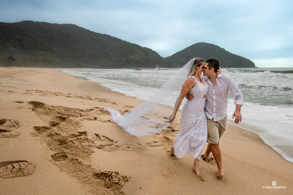 Noivos correndo se beijando pela areia da praia vermelha em Ubatuba, com seu véu voando durante ensaio pre wedding em ubatuba