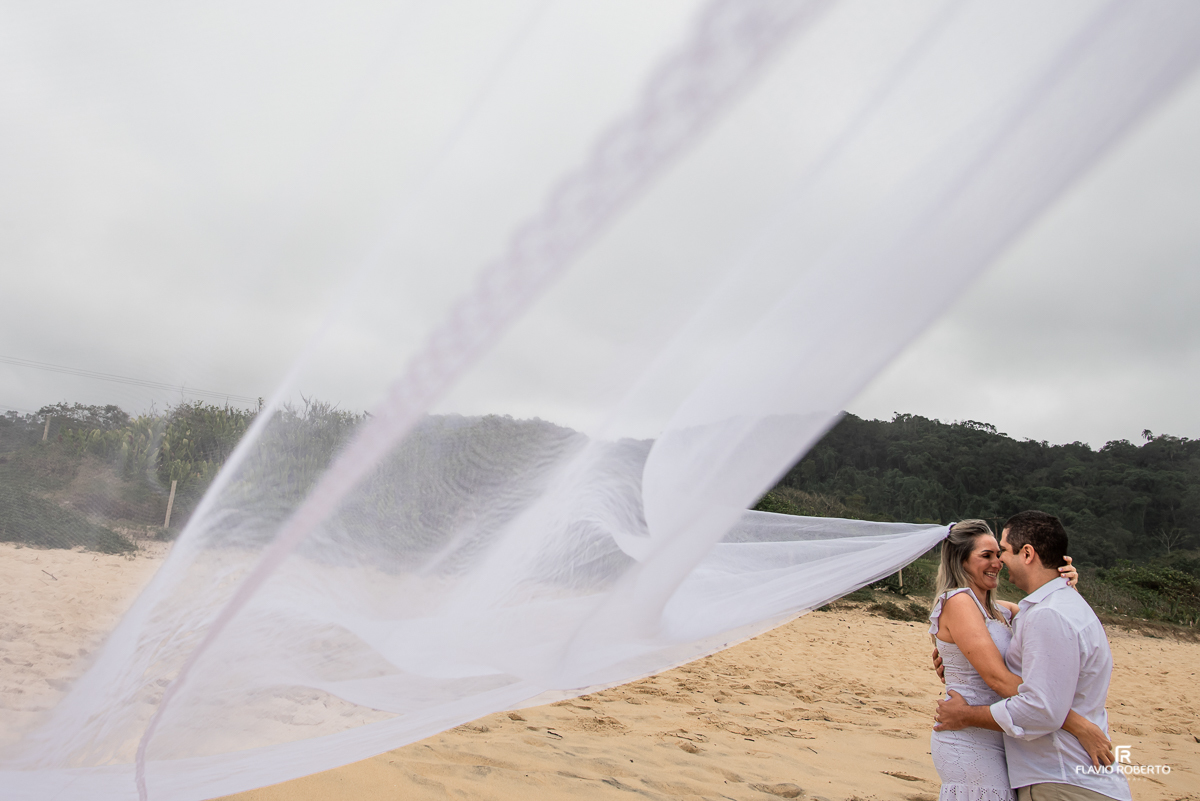 Noiva caminhando com seu noivo pela praia vermelha em Ubatuba, com seu véu voando durante ensaio pre wedding em ubatuba