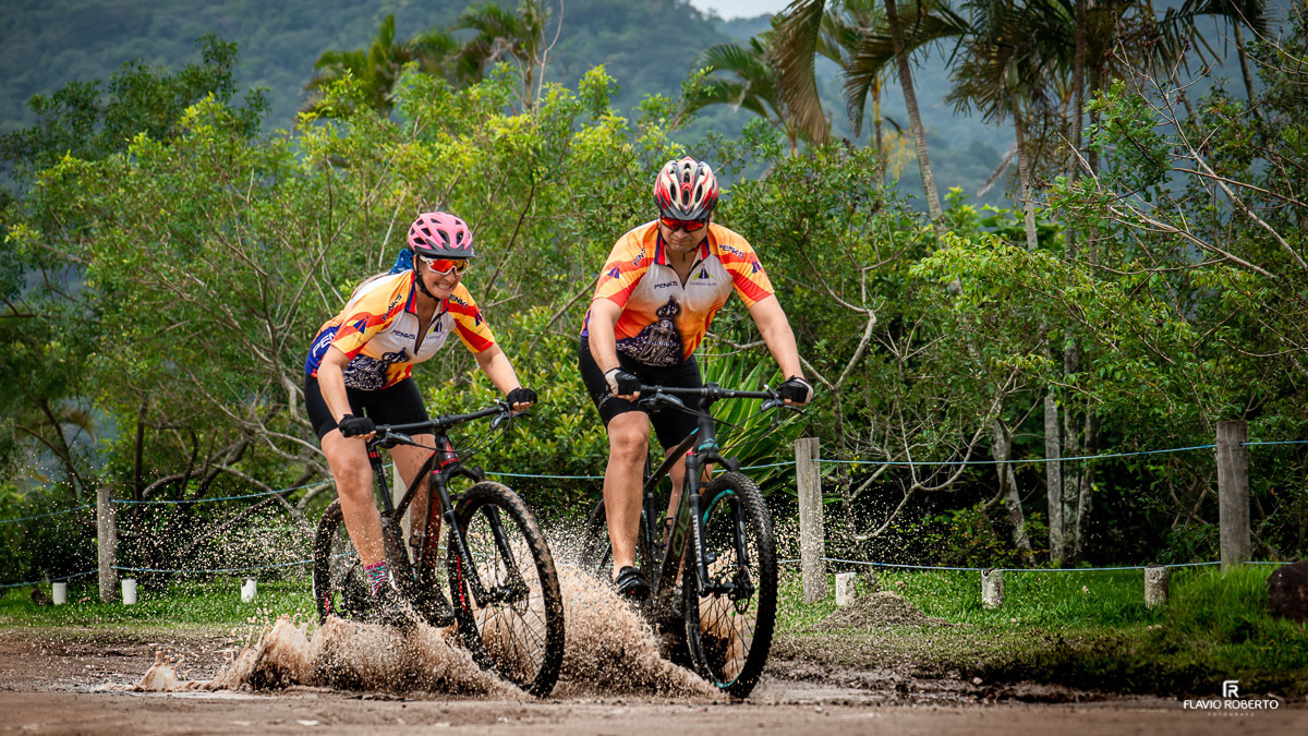 Casal pedalando sobre lama em trilha nas Ruínas de Lagoinha durante pré wedding aventureiro em Ubatuba.
