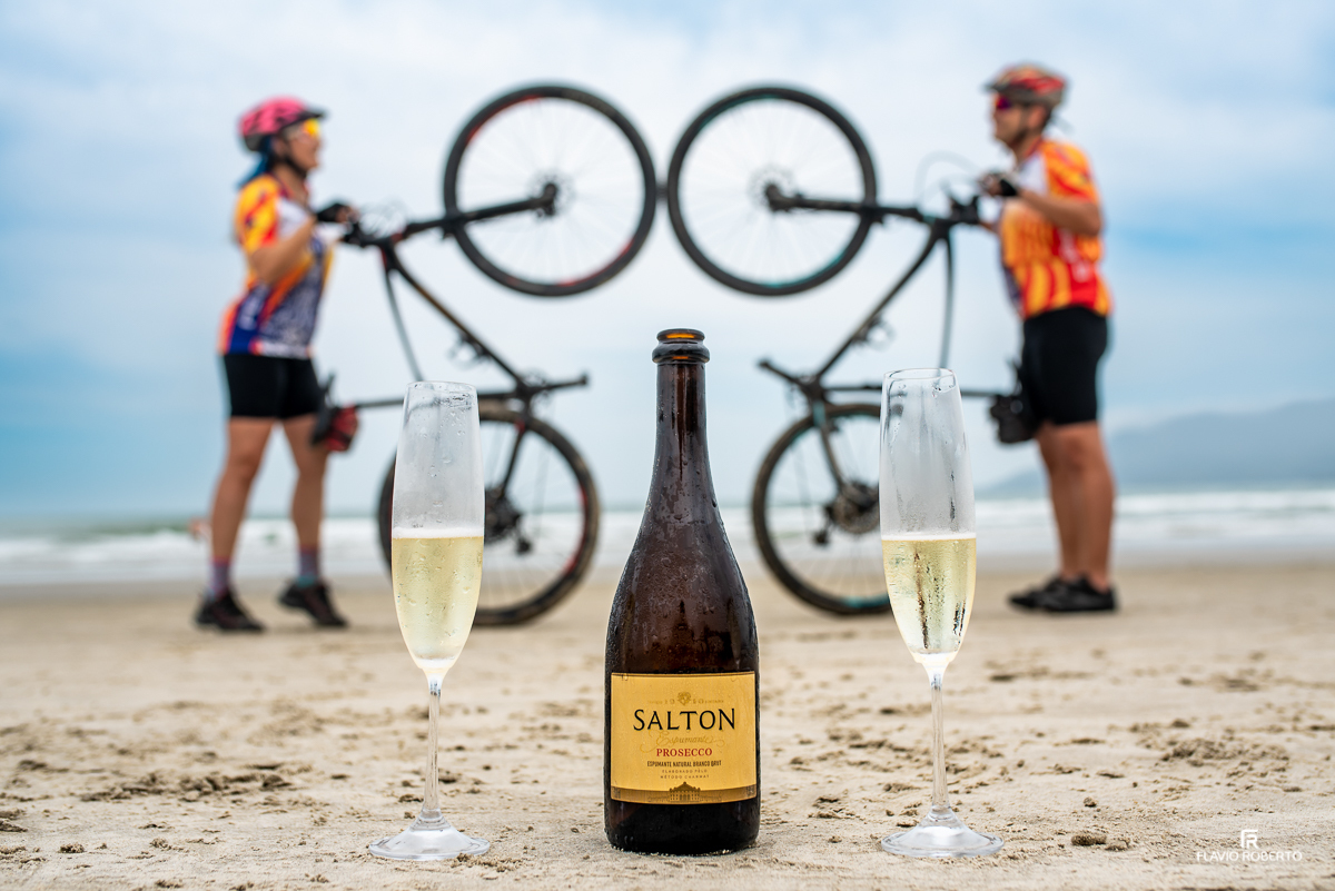 Casal de noivos ciclistas brindando com espumante na praia da Lagoinha em Ubatuba durante Ensaio Pre Wedding