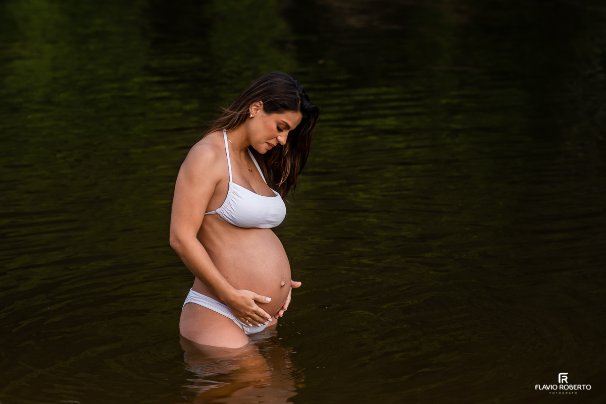 Mulher grávida olhando para sua barriga durante ensaio de gestante na praia de Ubatuba 