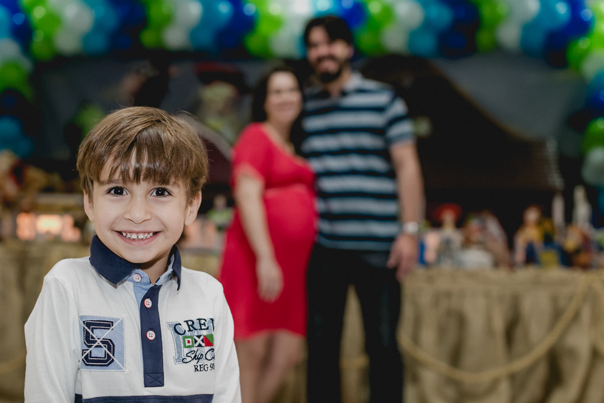 Pedro na frente da mesa do bolo com o papai e a mamae