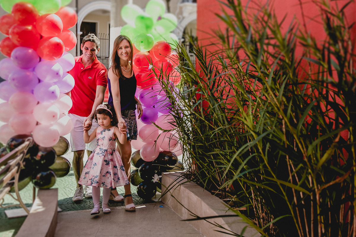 Alice chegando de mãos dadas com os pais para a festa de 3 anos