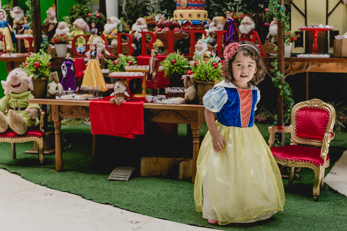 retrato da bibi vestida de branca de neve na frente da mesa do bolo