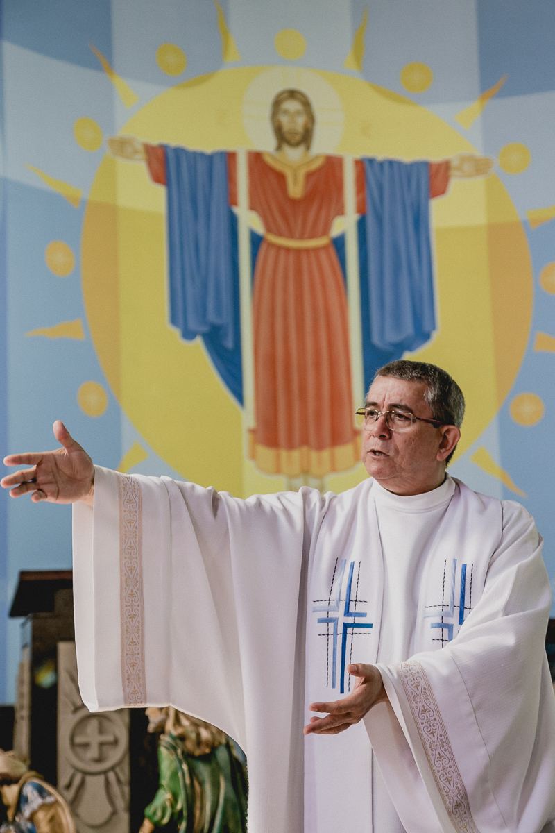 Padre discursando com a imagem ao fundo
